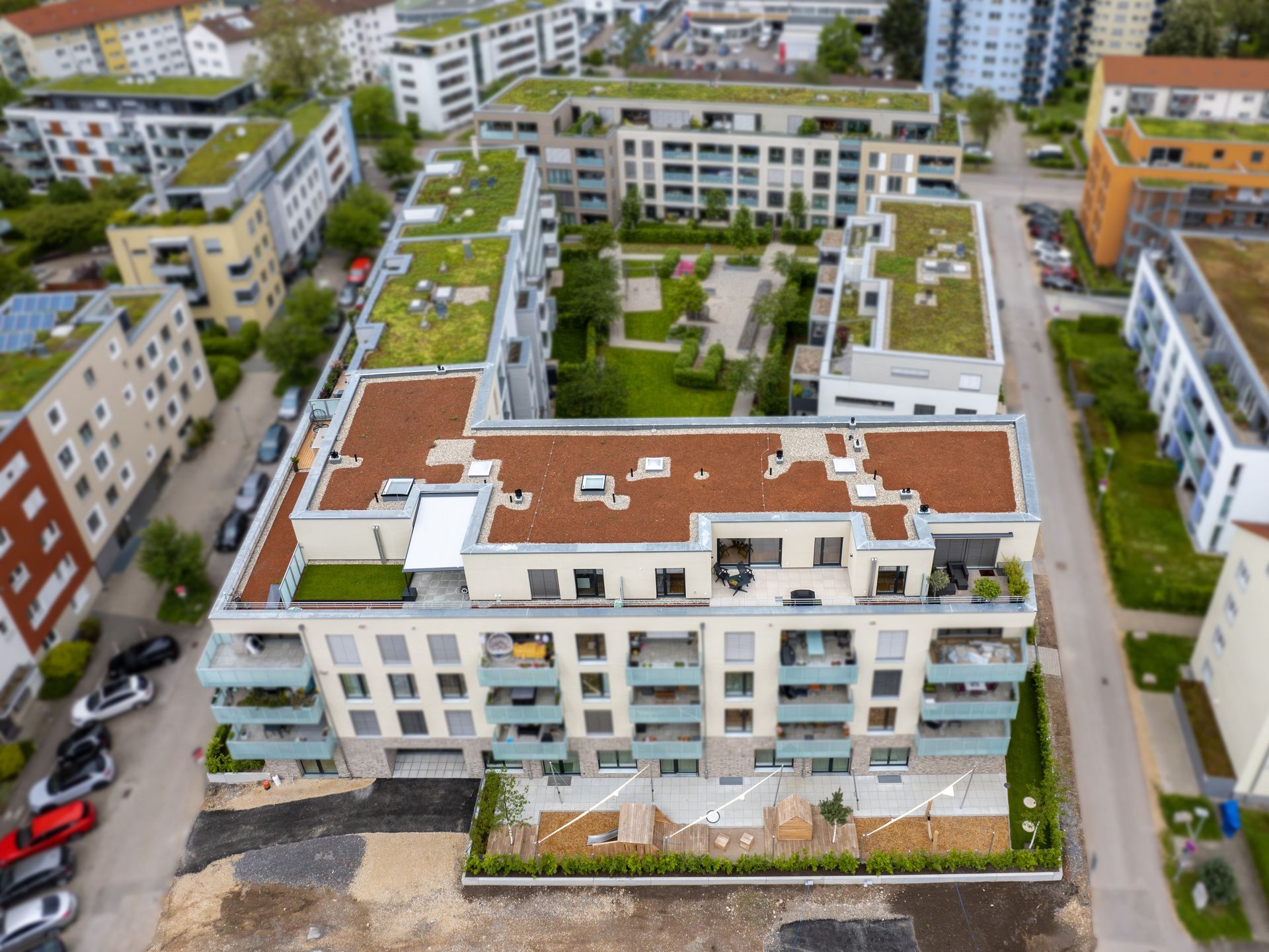 Das Bild zeigt eine moderne Wohnanlage mit begrünten Dächern und verschiedenen Gebäuden. Die Anlage ist von weiteren Häusern und viel Grün umgeben.