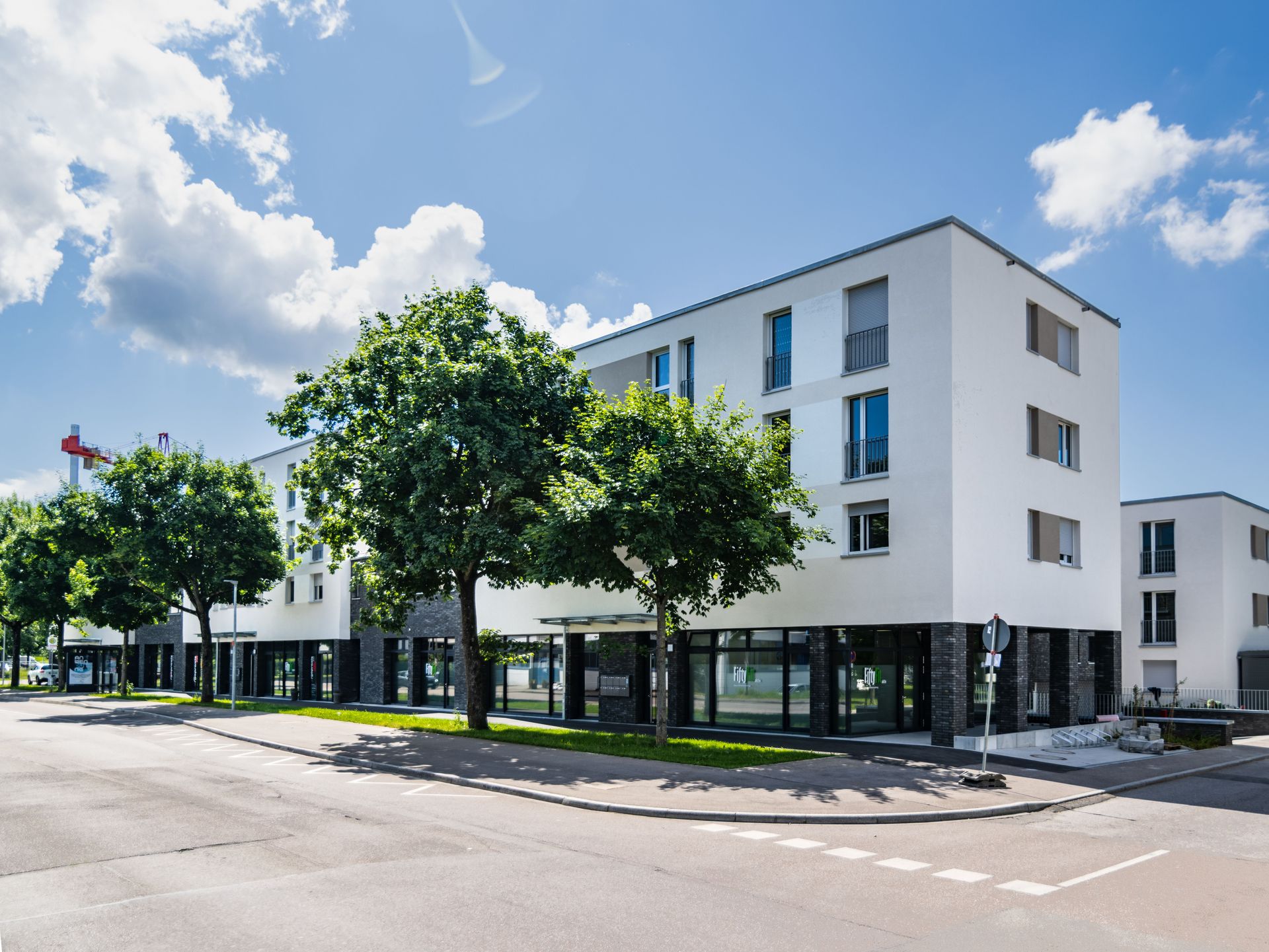 Das Bild zeigt mehrere Mehrfamilienhäuser mit weißer Fassade. Das Haus steht an einer Straße und vor dem Haus sind Bäume platziert.