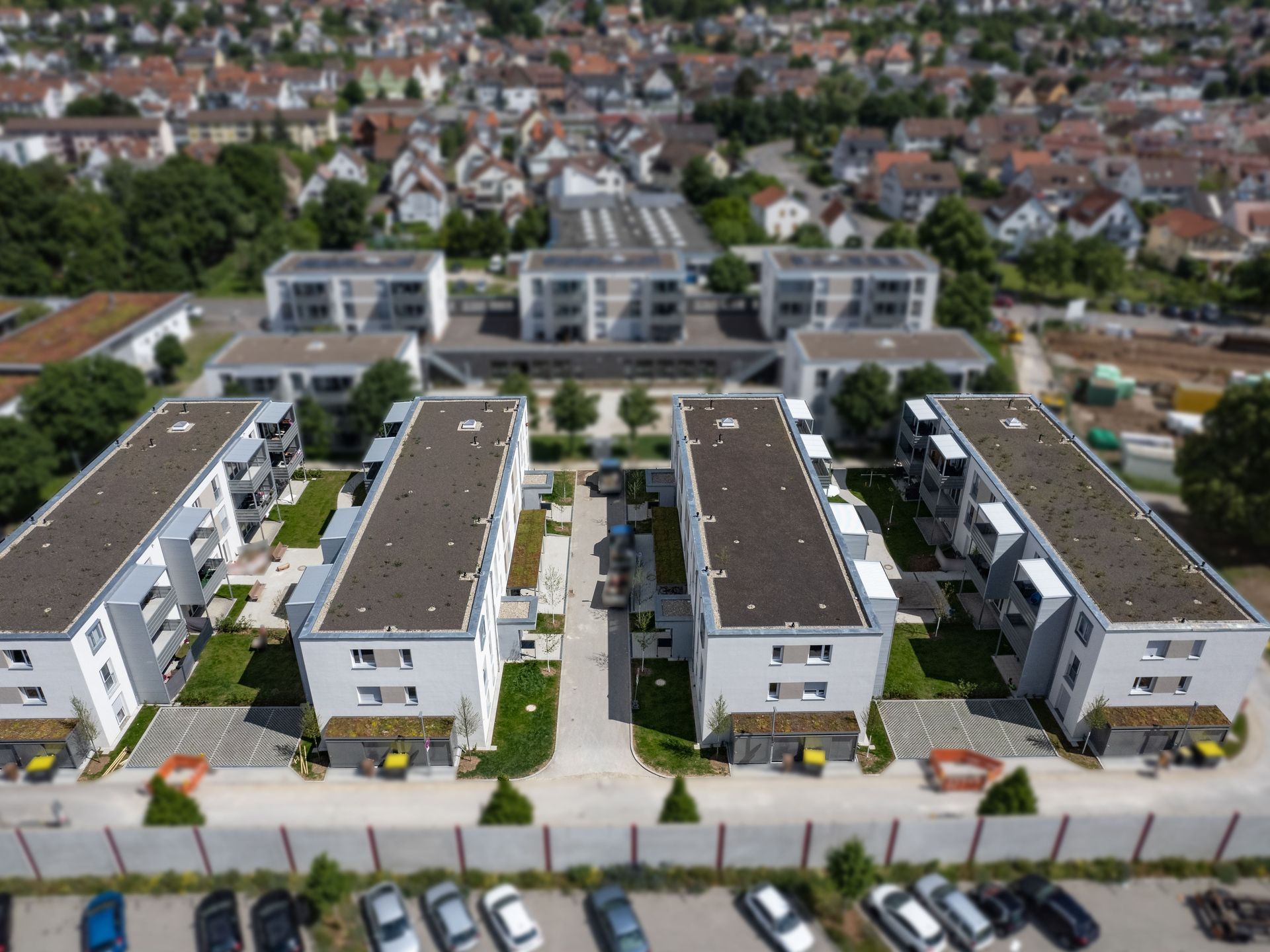 Das Bild zeigt eine Wohnanlage mit vier Mehrfamilienhäusern. Zwischen den Häusern führen Wege entlang und jedes Haus hat einen kleinen grünen Vorgarten.