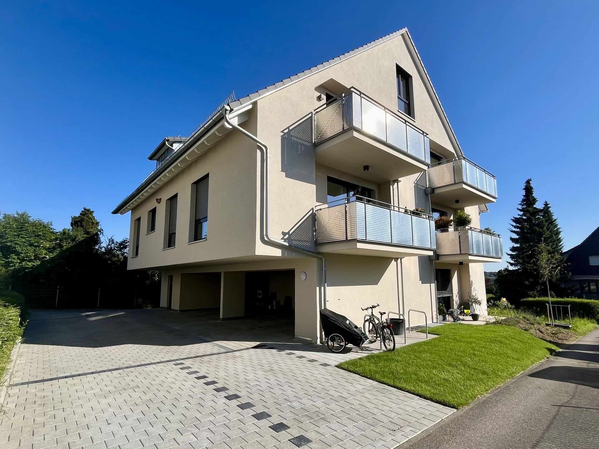 Das Bild zeigt ein Mehrfamilienhaus mit Balkonen. Vor dem Haus sieht man eine Rasenfläche und auch eine gepflasterte Fläche.