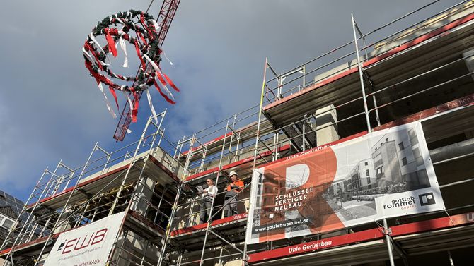 Das Bild zeigt ein Baugerüst an einem Haus. Außerdem sieht man dort noch einen Kranz zum Richtfest hängen.