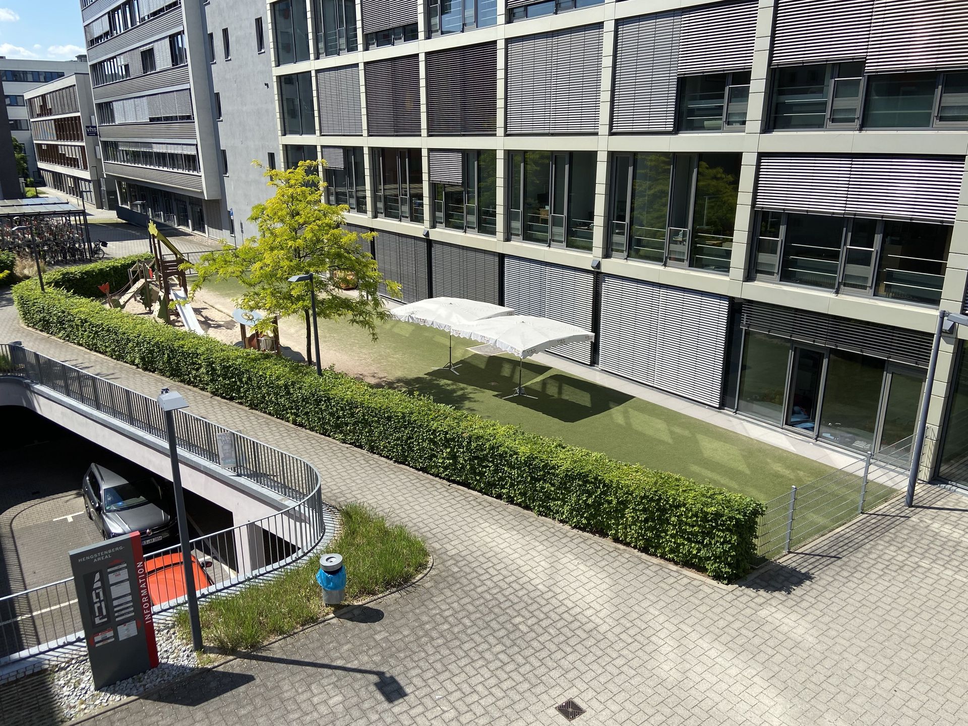 Das Bild zeigt eine Grünfläche mit Spielplatz neben einem Gebäude.