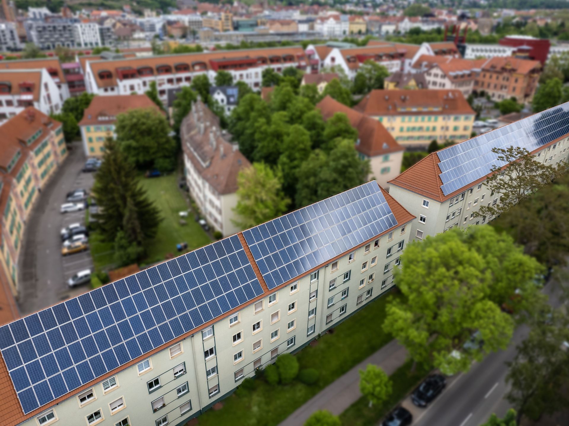 Das Bild zeigt eine Dachfläche mit Solaranlage auf einem Mehrfamilienhaus. Das Haus ist von Bäumen und anderen Gebäuden umgeben.