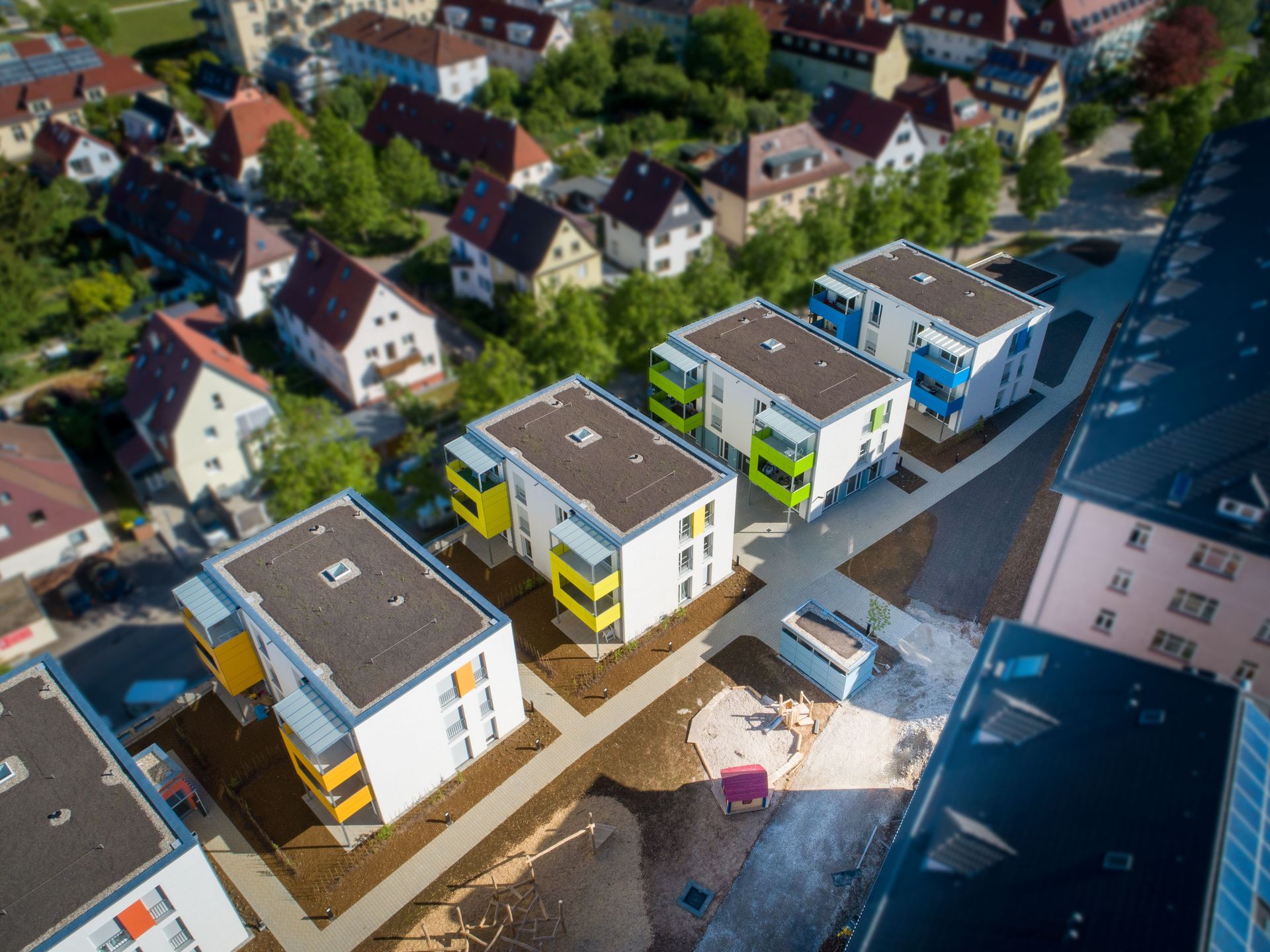Das Bild zeigt mehrere Mehrfamilienhäuser mit weißer Fassade und bunten Balkonen. An den Häusern führen Wege vorbei.