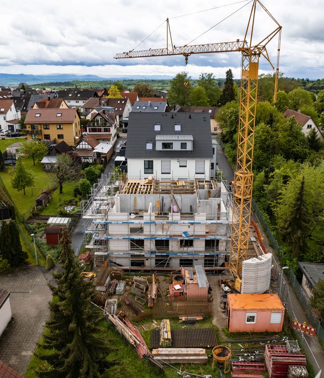 Das Bild zeigt eine Baustelle eines Hauses. Vor dem Haus sieht man einen Baukran und Baumaterialien. Link zum Bereich Baugemeinschaftsprojekte.