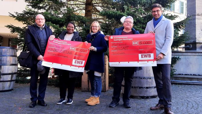 Das Bild zeigt fünf Personen, die zwei Spendenchecks halten. Im Hintergrund sieht man einen Baum.