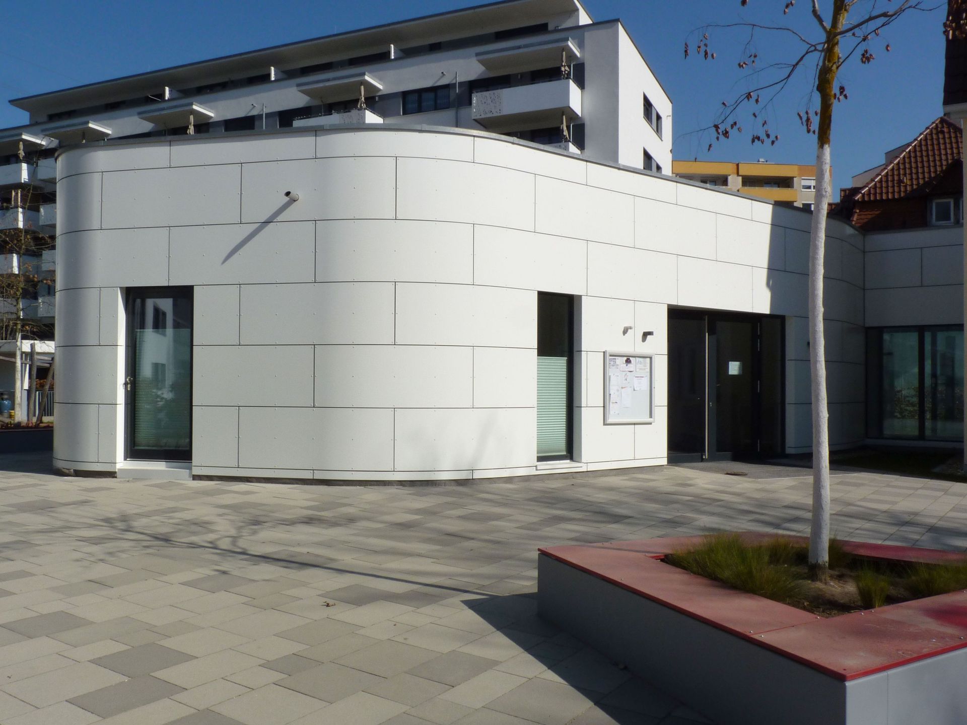 Das Bild zeigt ein Gebäude mit heller Fassade und eine Sitzmöglichkeit.