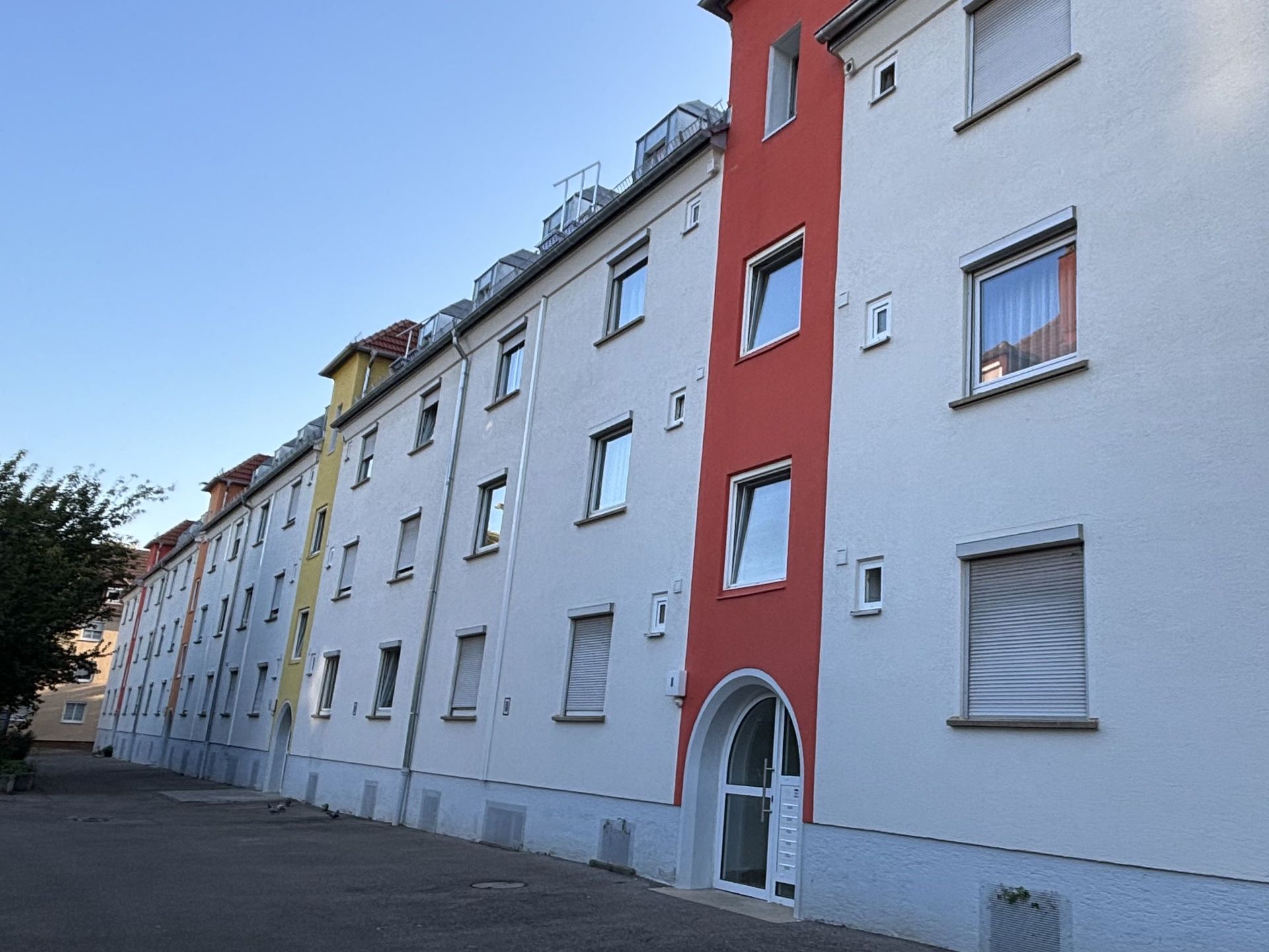 Das Bild zeigt eine Reihe von Mehrfamilienhäusern mit weißer Fassade, die durch farbige Akzente an einzelnen Gebäudeteilen aufgelockert wird. Die Häuser haben mehrere Stockwerke und sind mit Fenstern und Türen ausgestattet.