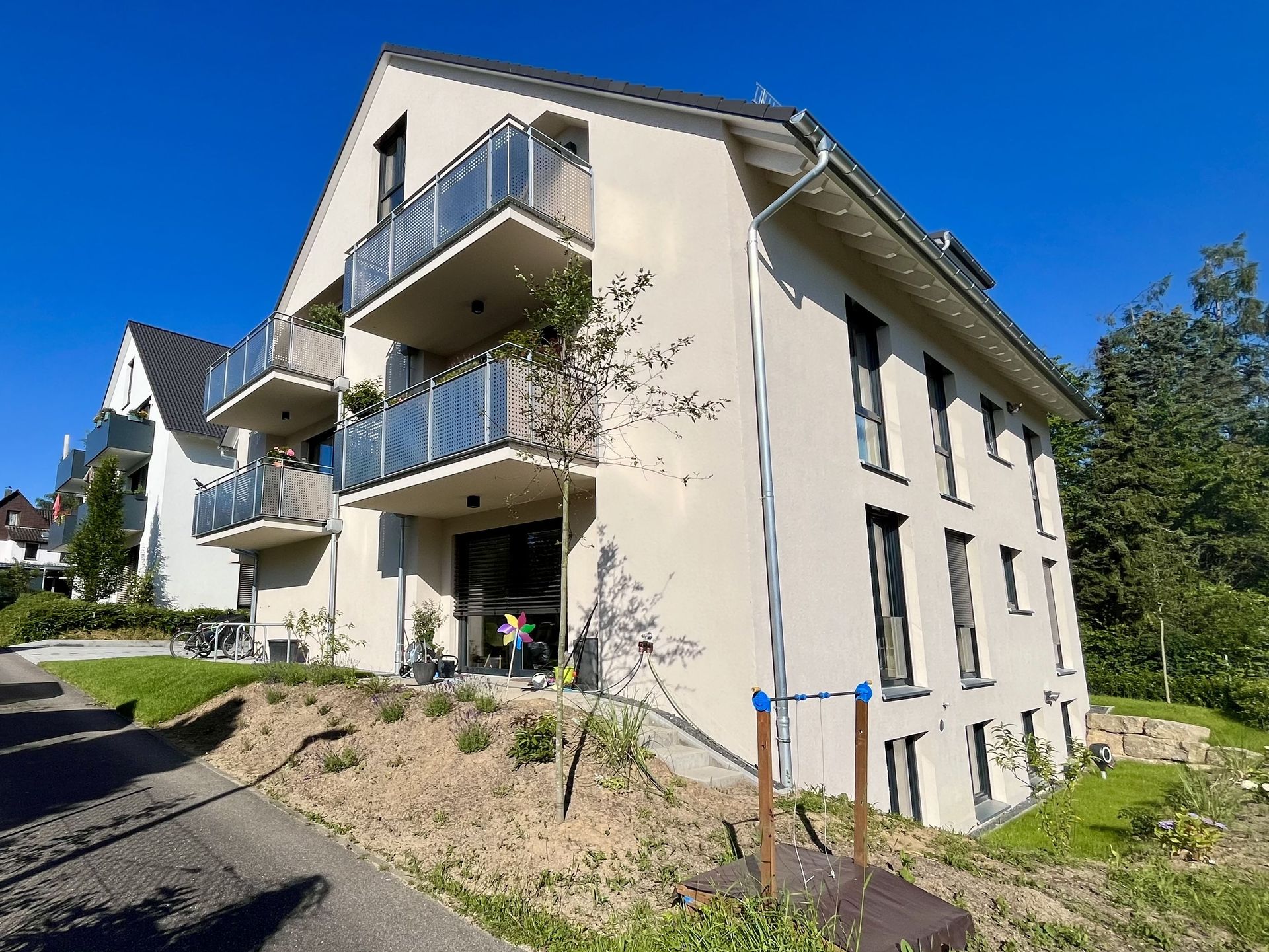 Das Bild zeigt ein Mehrfamilienhaus mit heller Fassade und einer Grünfläche um das Haus herum.