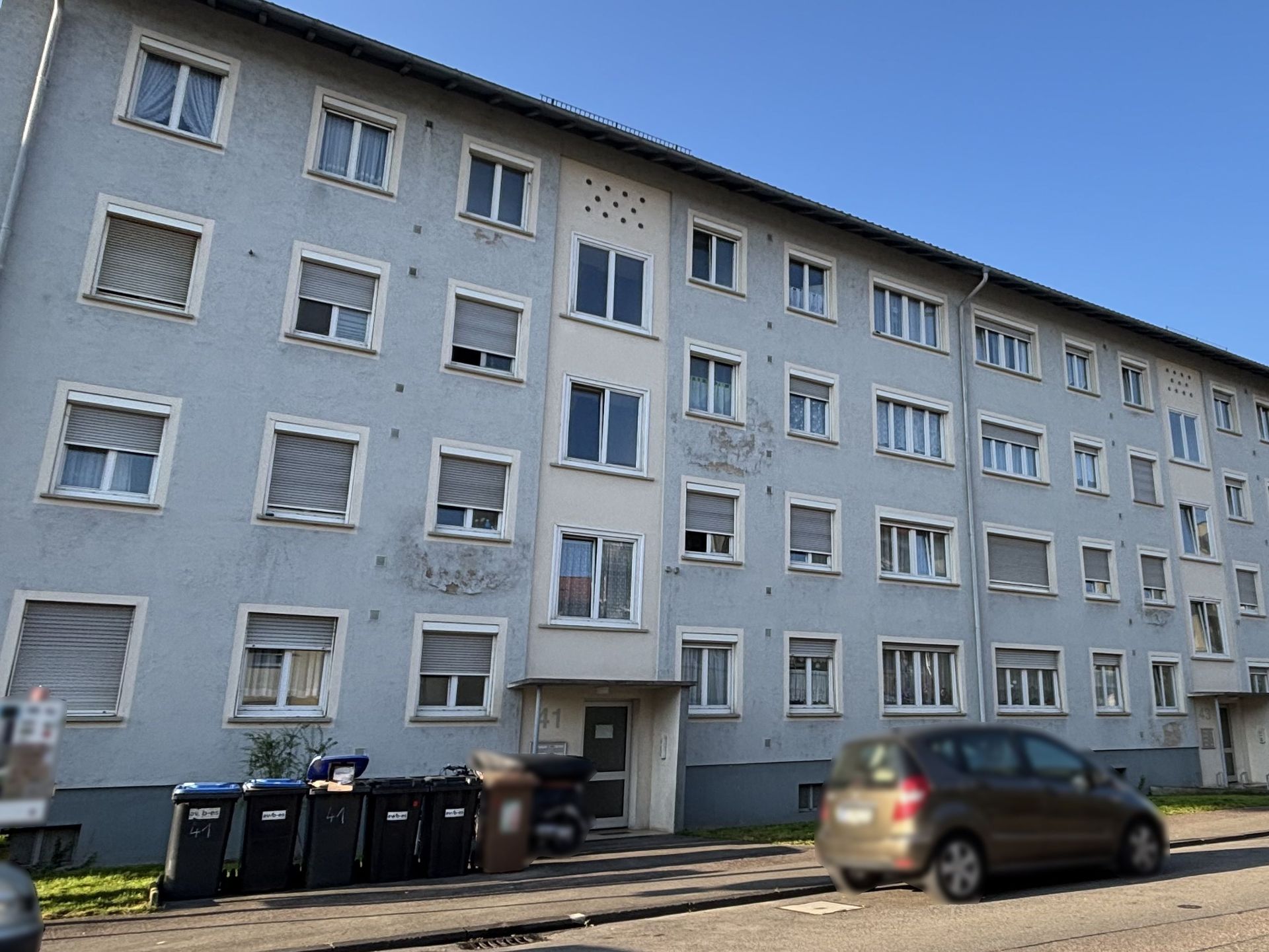 Das Bild zeigt ein Mehrfamilienhaus mit hellblauer Fassade und mehreren Stockwerken.