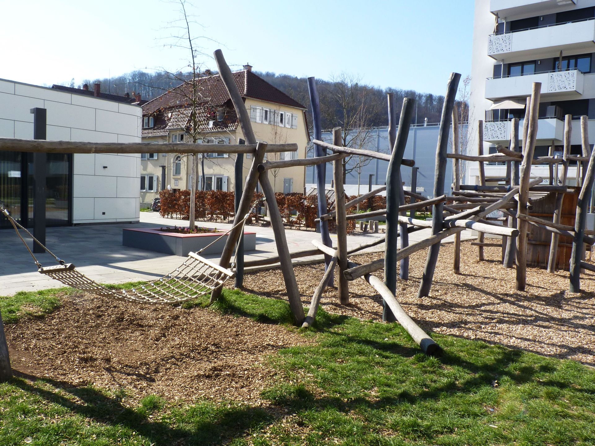 Das Bild zeigt einen Spielplatz. Dahinter befindet sich ein Gebäude.