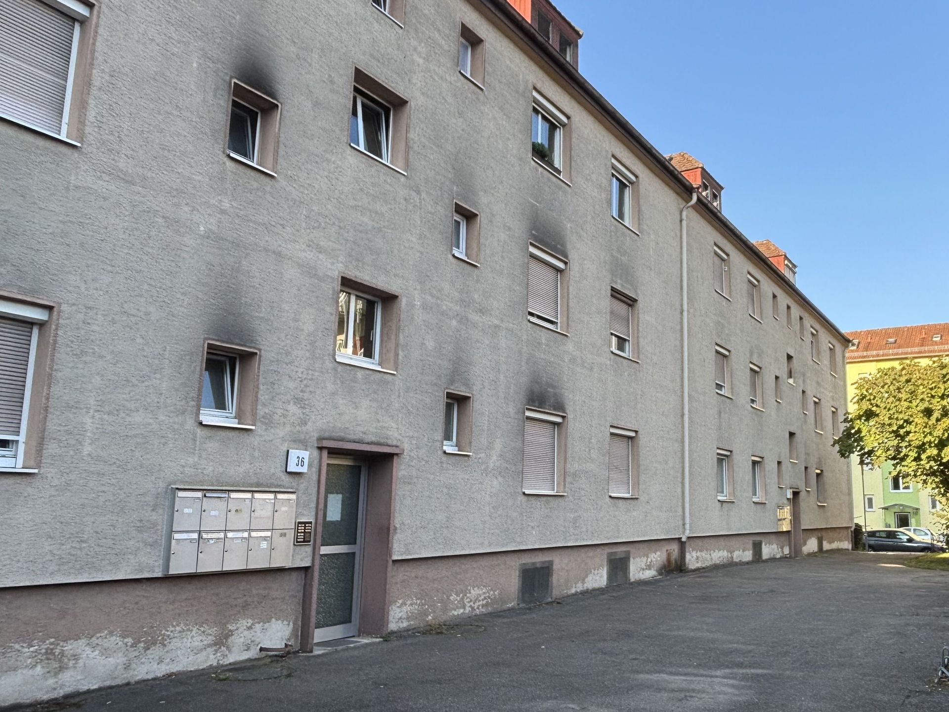 Das Bild zeigt ein Mehrfamilienhaus mit grauer Fassade. Die Fassade weist an einigen Stellen dunkle Verfärbungen auf.