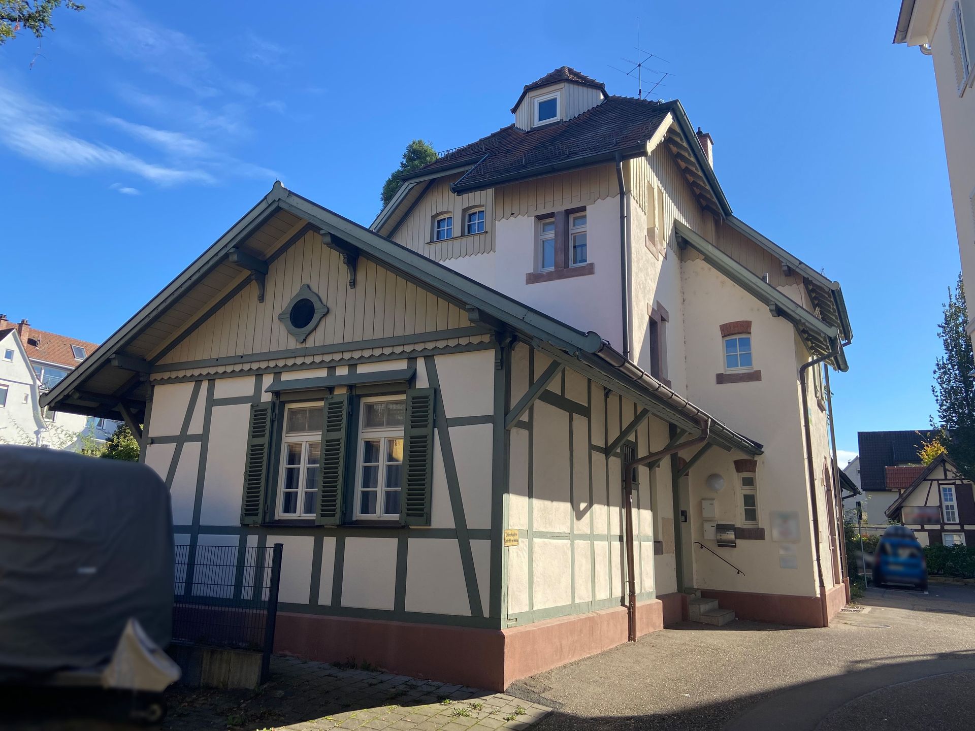 Das Bild zeigt ein Gebäude mit Fachwerk-Optik. Das Haus hat ein Dach mit Dachgauben und grüne Fensterläden.
