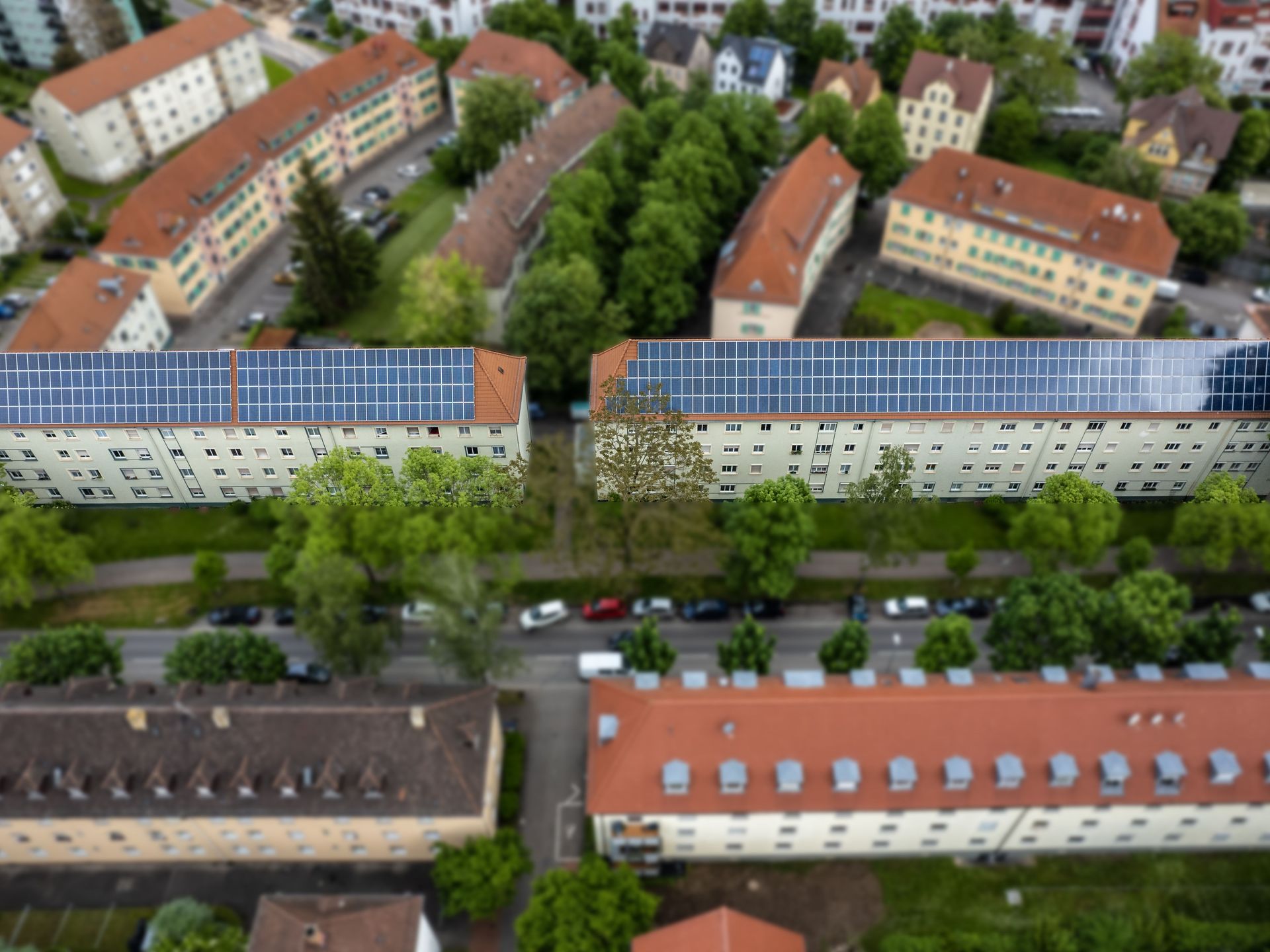 Das Bild zeigt eine Luftaufnahme von mehreren Gebäuden mit Solaranlagen auf den Dächern. Die Gebäude befinden sich in einer Umgebung mit vielen weiteren Häusern und Straßen.