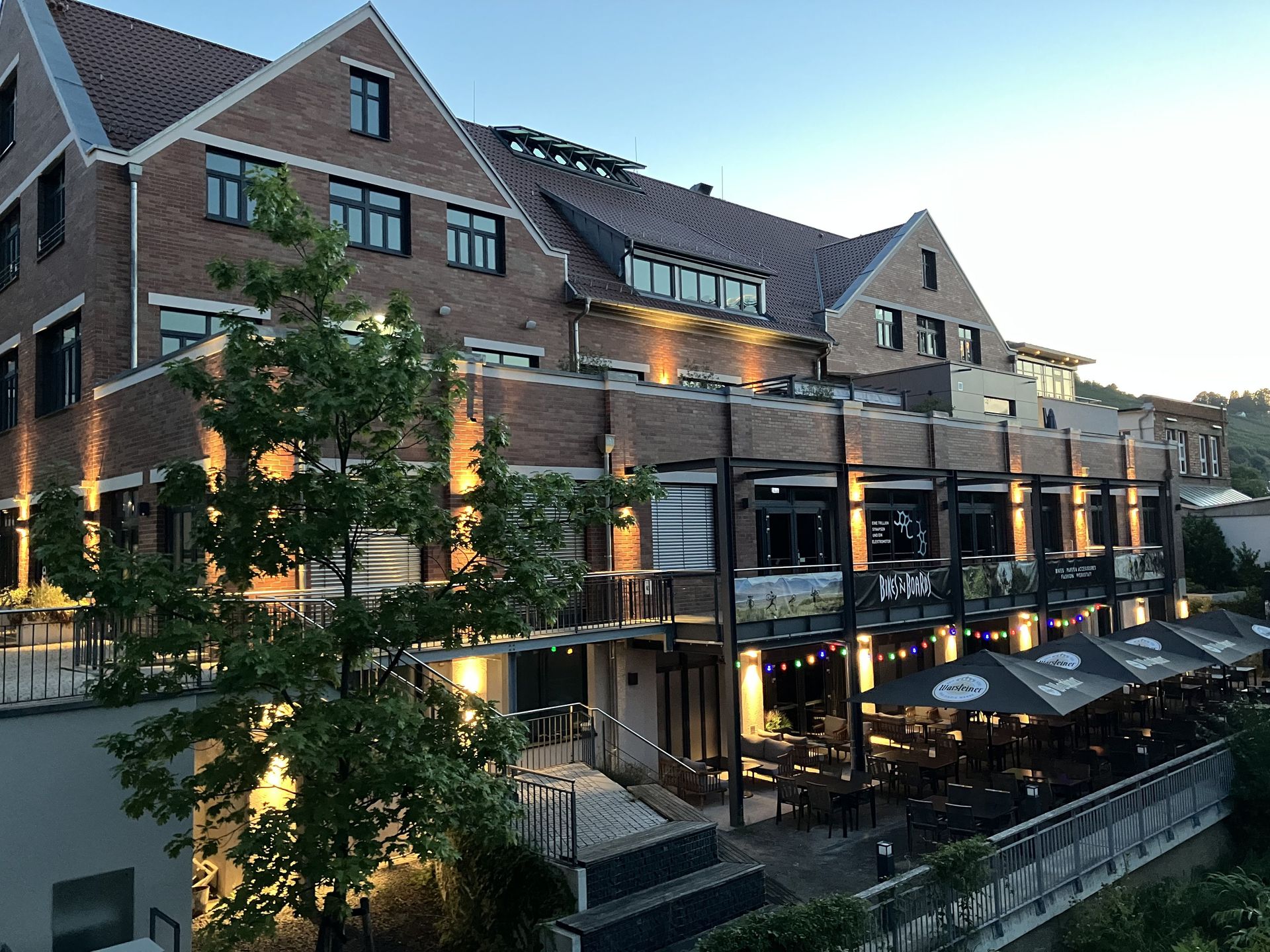 Das Bild zeigt ein Gebäudekomplex mit verschiedenen Büroräumen direkt am Neckar. Man sieht viele Sitzgelegenheiten.