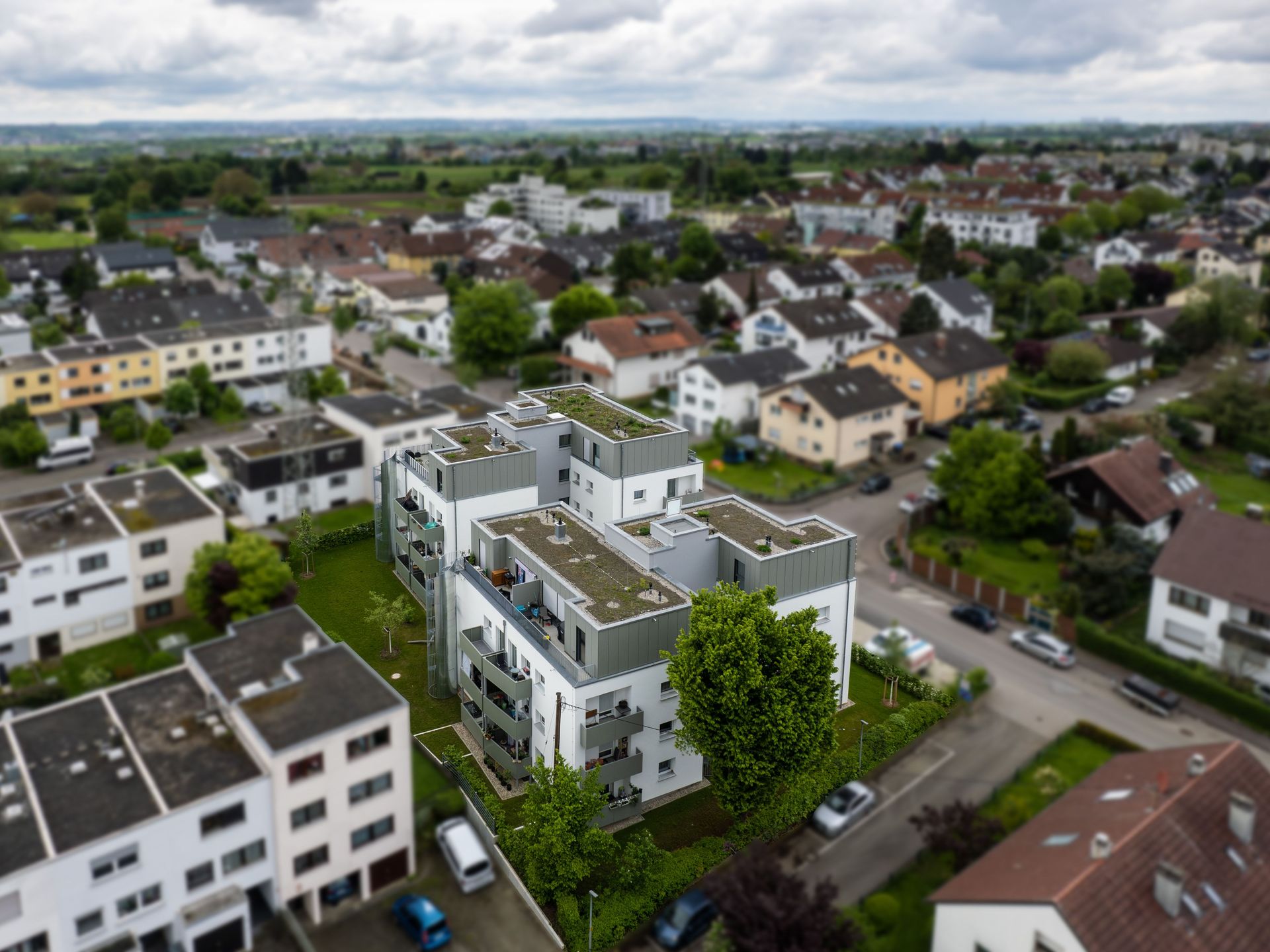 Das Bild zeigt eine Luftaufnahme eines Wohngebiets mit einer Mischung aus Mehrfamilienhäusern und Einfamilienhäusern. Einige Dächer sind begrünt.
