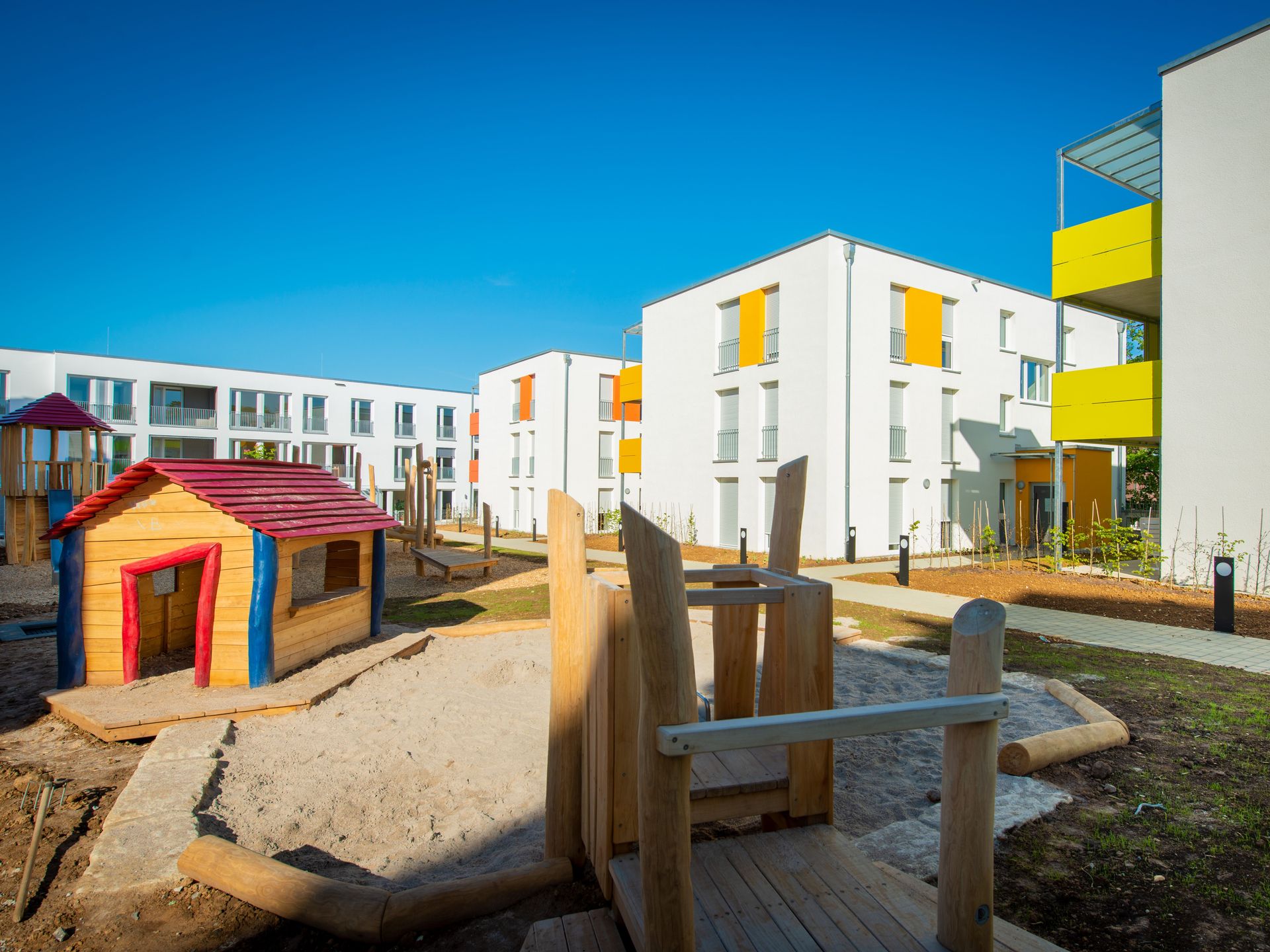 Das Bild zeigt eine Wohnanlage mit Häusern, die bunte Balkone besitzen. Im Vordergrund sieht man einen Spielplatz.