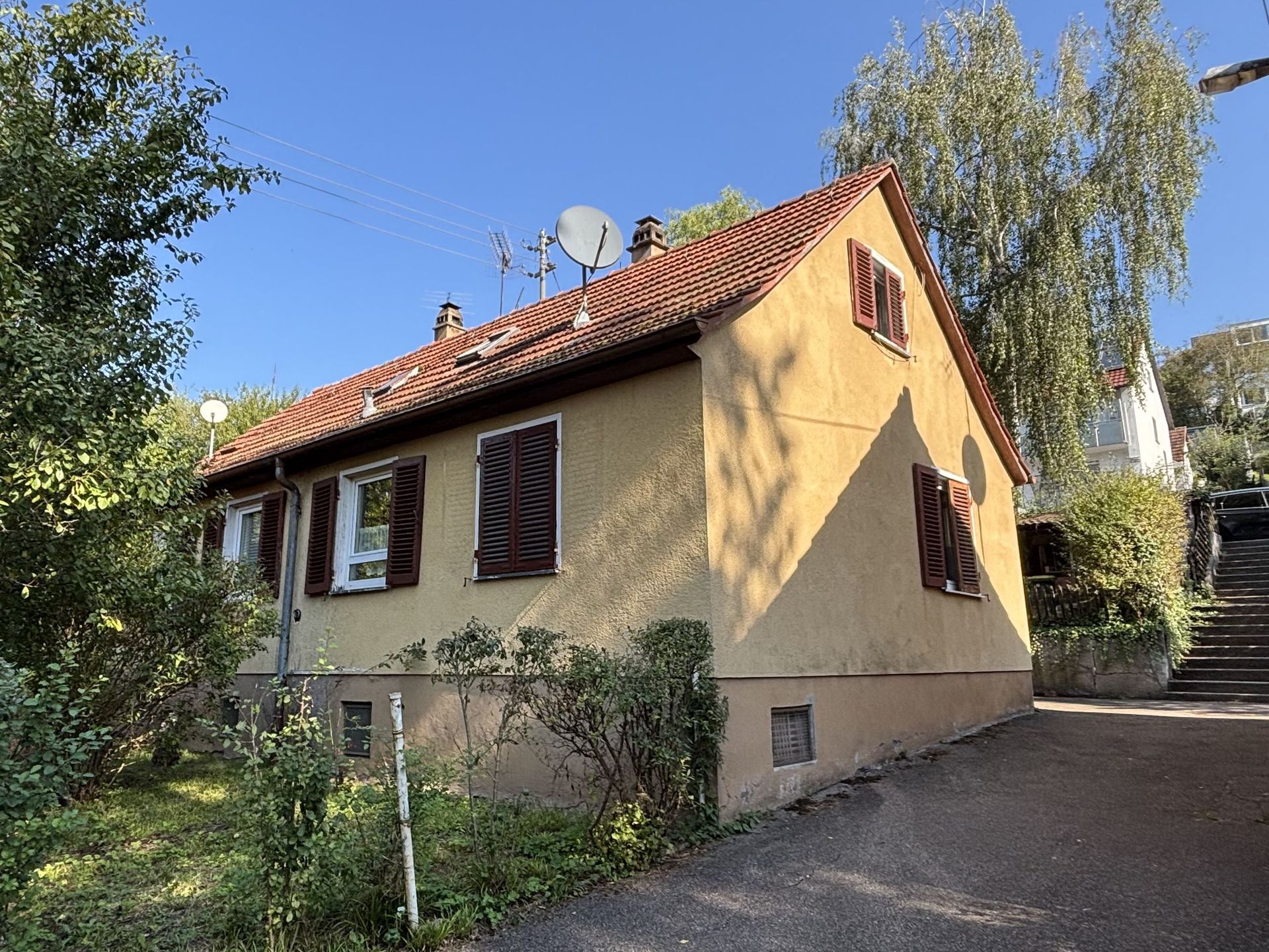 Das Bild zeigt ein freistehendes Haus mit Garten. Das Haus hat eine helle Fassade, ein rotes Dach und braune Fensterläden.