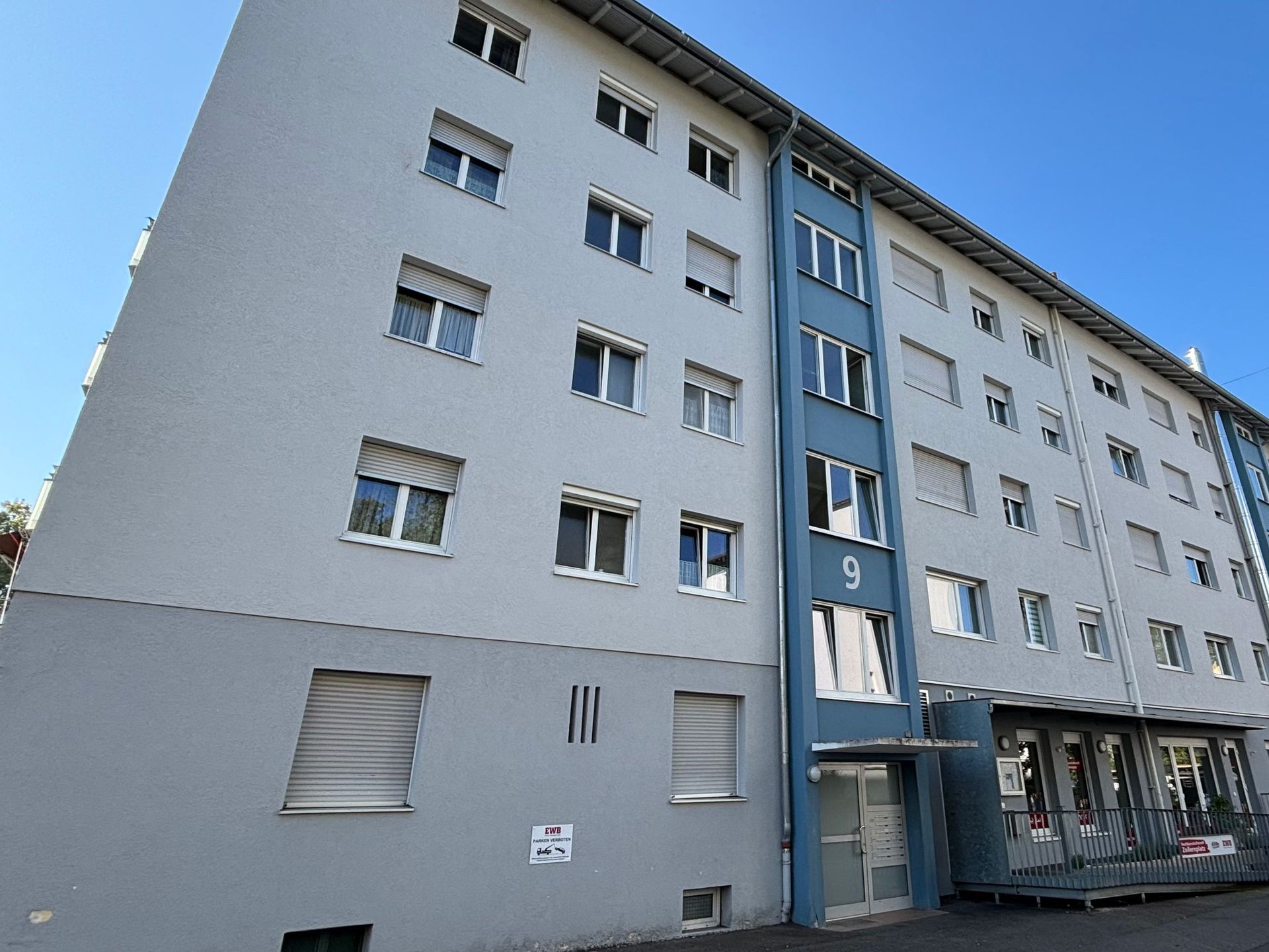 Das Bild zeigt ein Mehrfamilienhaus mit heller Fassade und blauen Elementen.