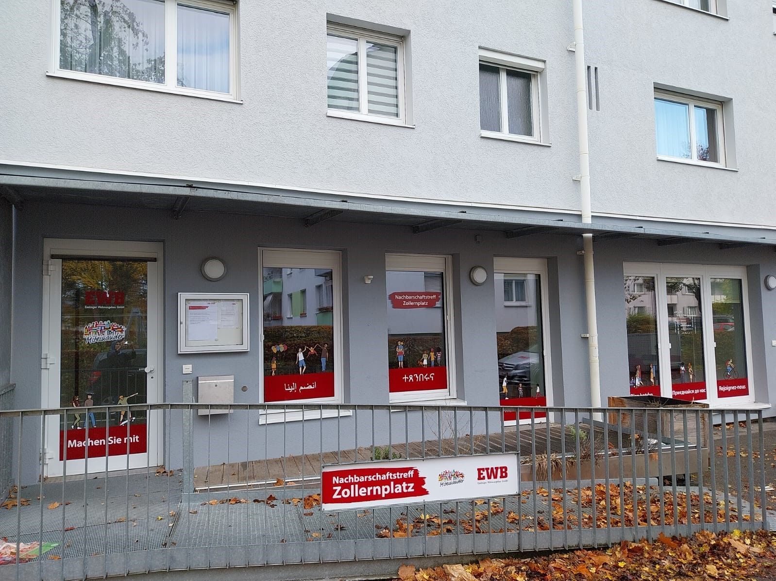 Das Bild zeigt eine Fensterfront, die mit Gestaltungselementen beklebt ist. Außerdem sieht man auch ein Geländer, an dem ein Schild befestigt ist.