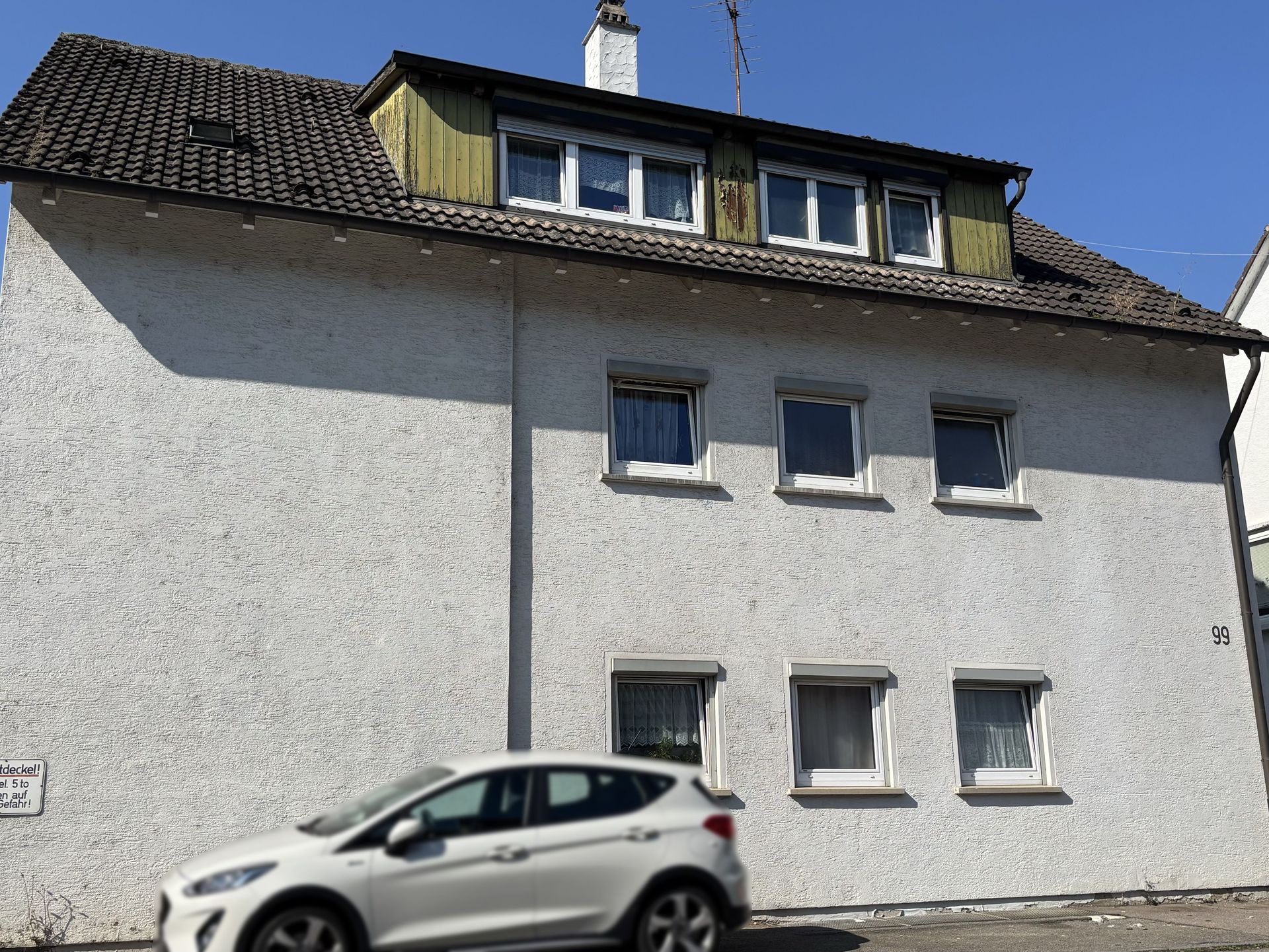 Das Bild zeigt ein mehrstöckiges Haus mit heller Fassade. Das Haus hat ein ausgebautes Dachgeschoss mit mehreren Fenstern.