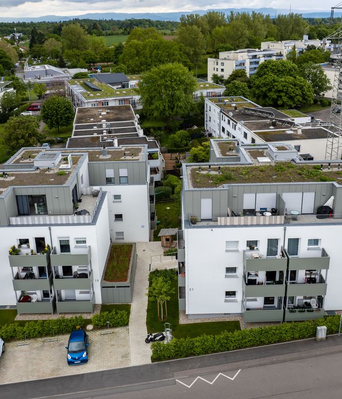 Das Bild zeigt eine Wohnanlage mit mehreren Mehrfamilienhäusern. Die Fassaden sind weiß und die Balkone grau. Link zum Bereich Aufstockung/Modernisierung.