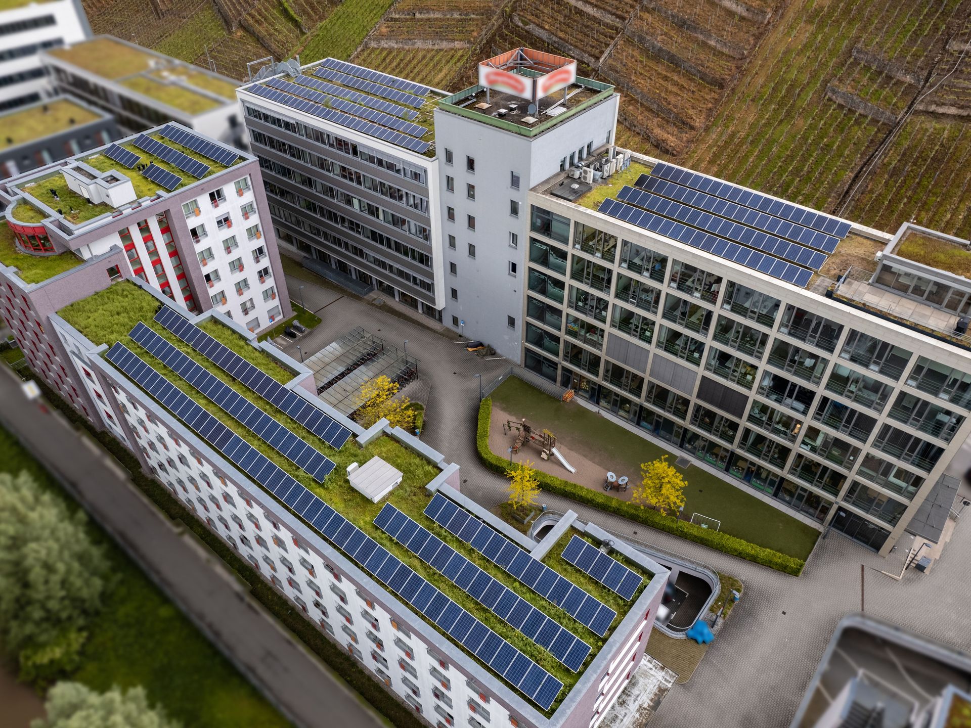 Das Bild zeigt mehrere Gebäude, die mit Solaranlagen bedeckt sind. Zwischen den Häusern befindet sich ein Innenhof mit Spielplatz und Grünflächen.