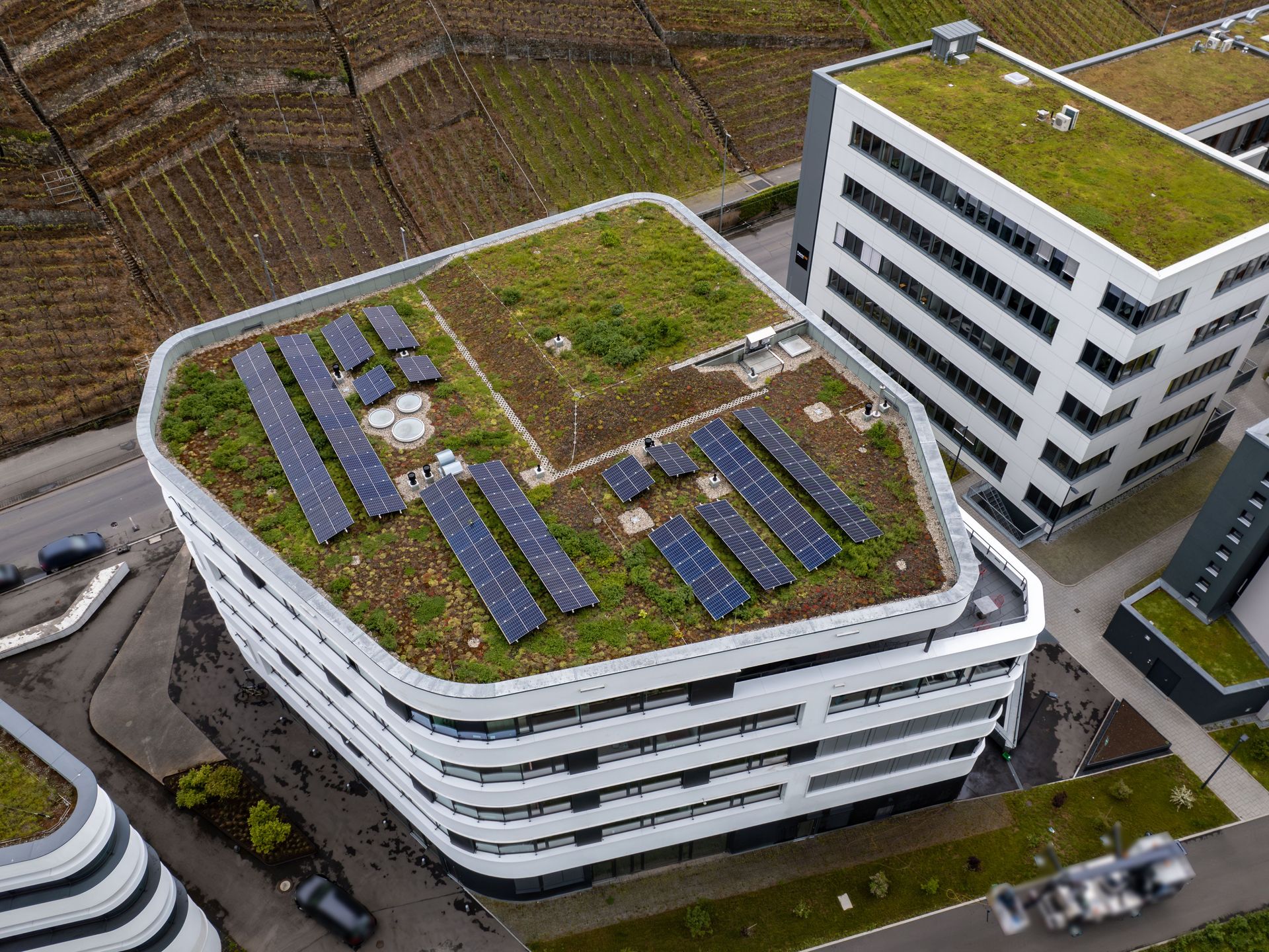 Das Bild zeigt ein modernes Gebäude mit begrüntem Dach und einer großen Solaranlage. Das Gebäude hat eine geschwungene Form und weiße Fassadenelemente.