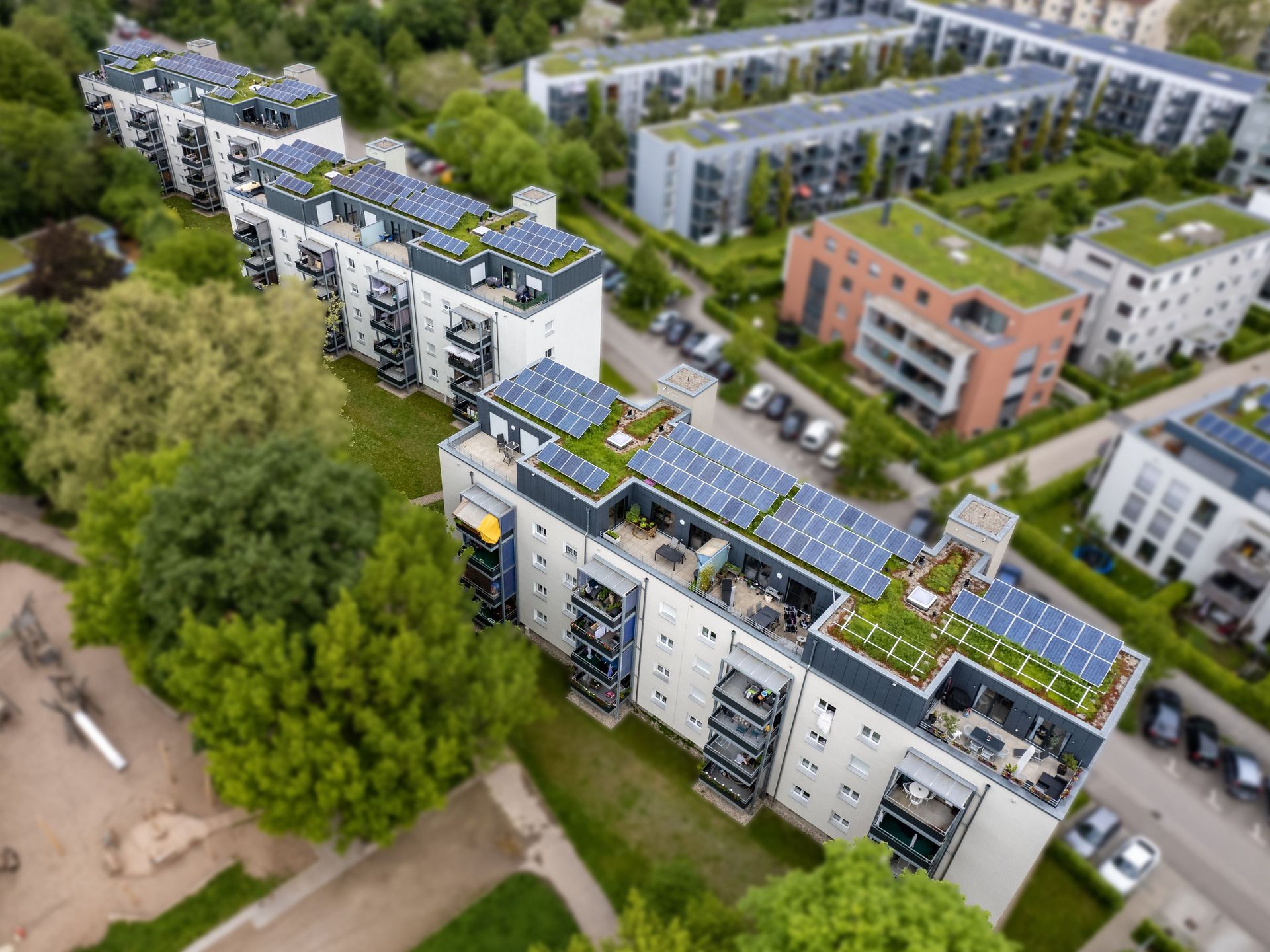 Das Bild zeigt eine Luftaufnahme einer Wohnanlage mit mehreren Gebäuden und begrünten Dächern. Auf einigen Dächern sind Solaranlagen installiert.