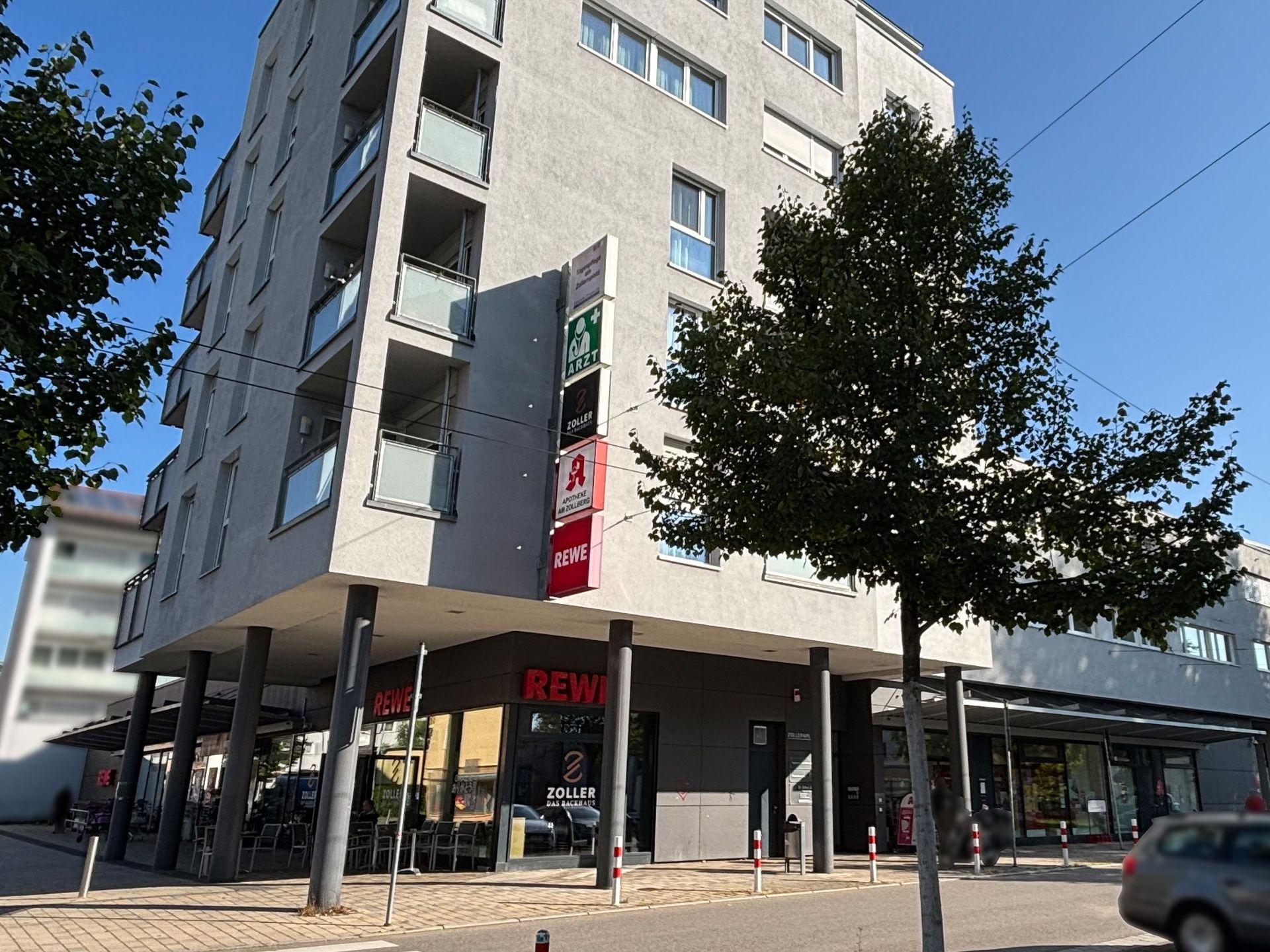 Das Bild zeigt ein modernes Gebäude mit einem Supermarkt im Erdgeschoss. Über dem Supermarkt befinden sich mehrere Stockwerke mit Wohnungen oder Büros.