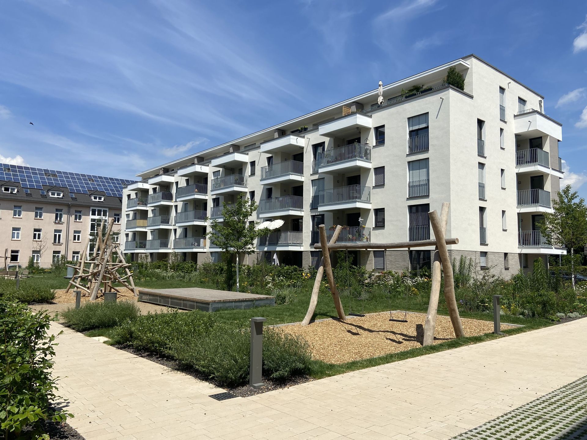Das Bild zeigt ein mehrstöckiges Wohnhaus. Vor dem Haus sind ein Spielplatz und Grünflächen.