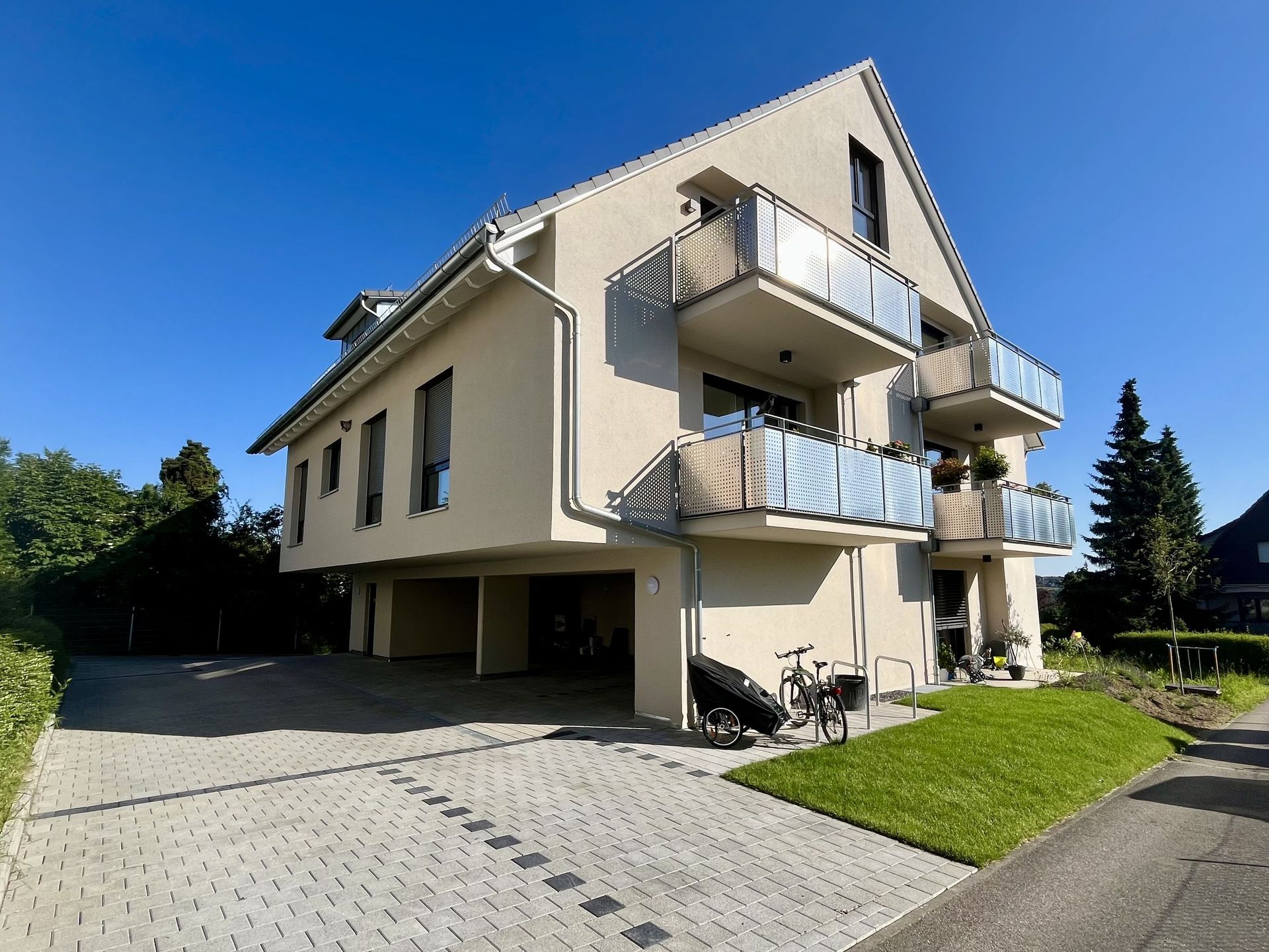 Das Bild zeigt ein Mehrfamilienhaus mit Balkonen. Vor dem Haus sieht man eine Rasenfläche und auch eine gepflasterte Fläche.